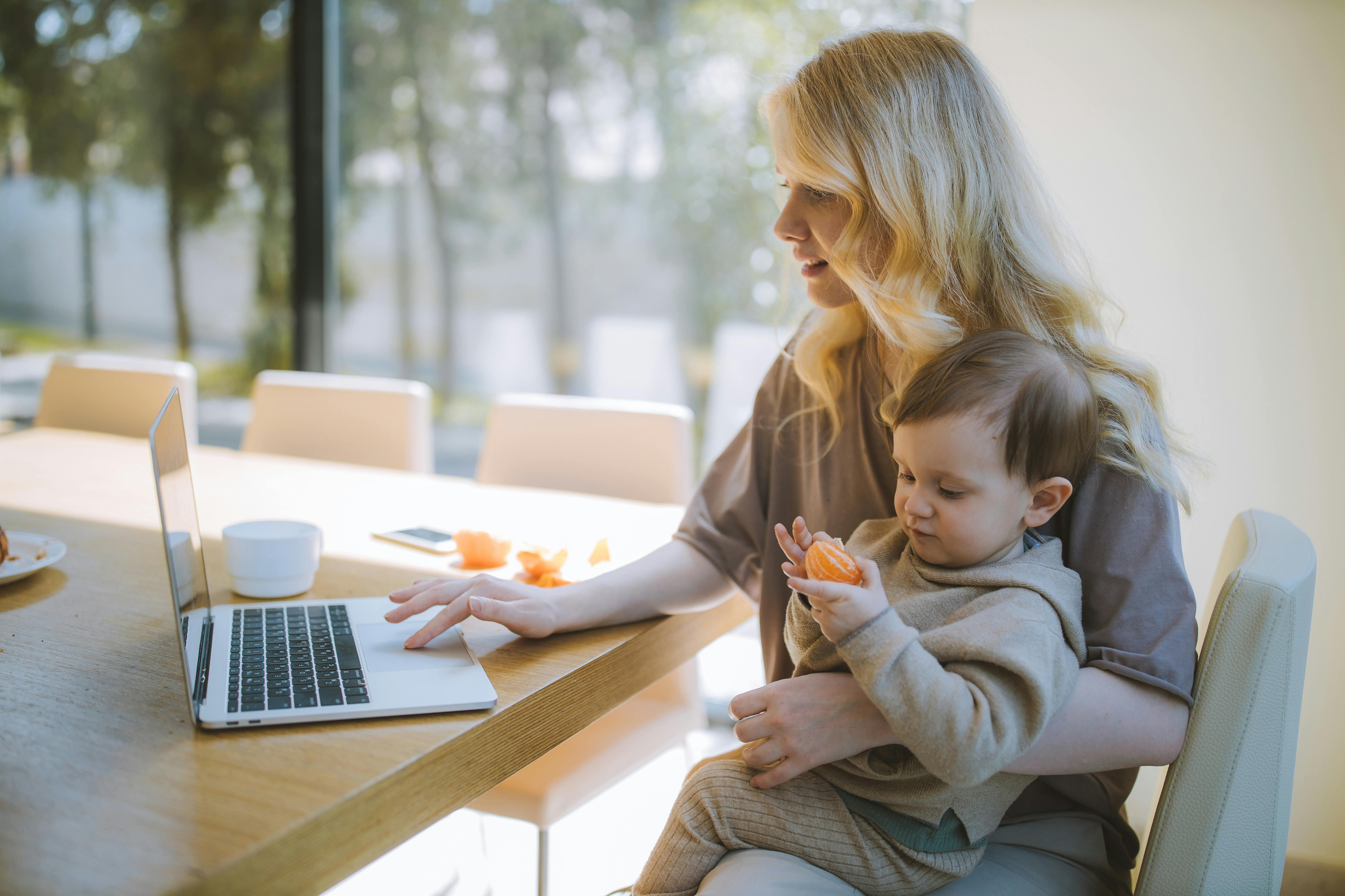 Mother working on laptop at home while holding her baby